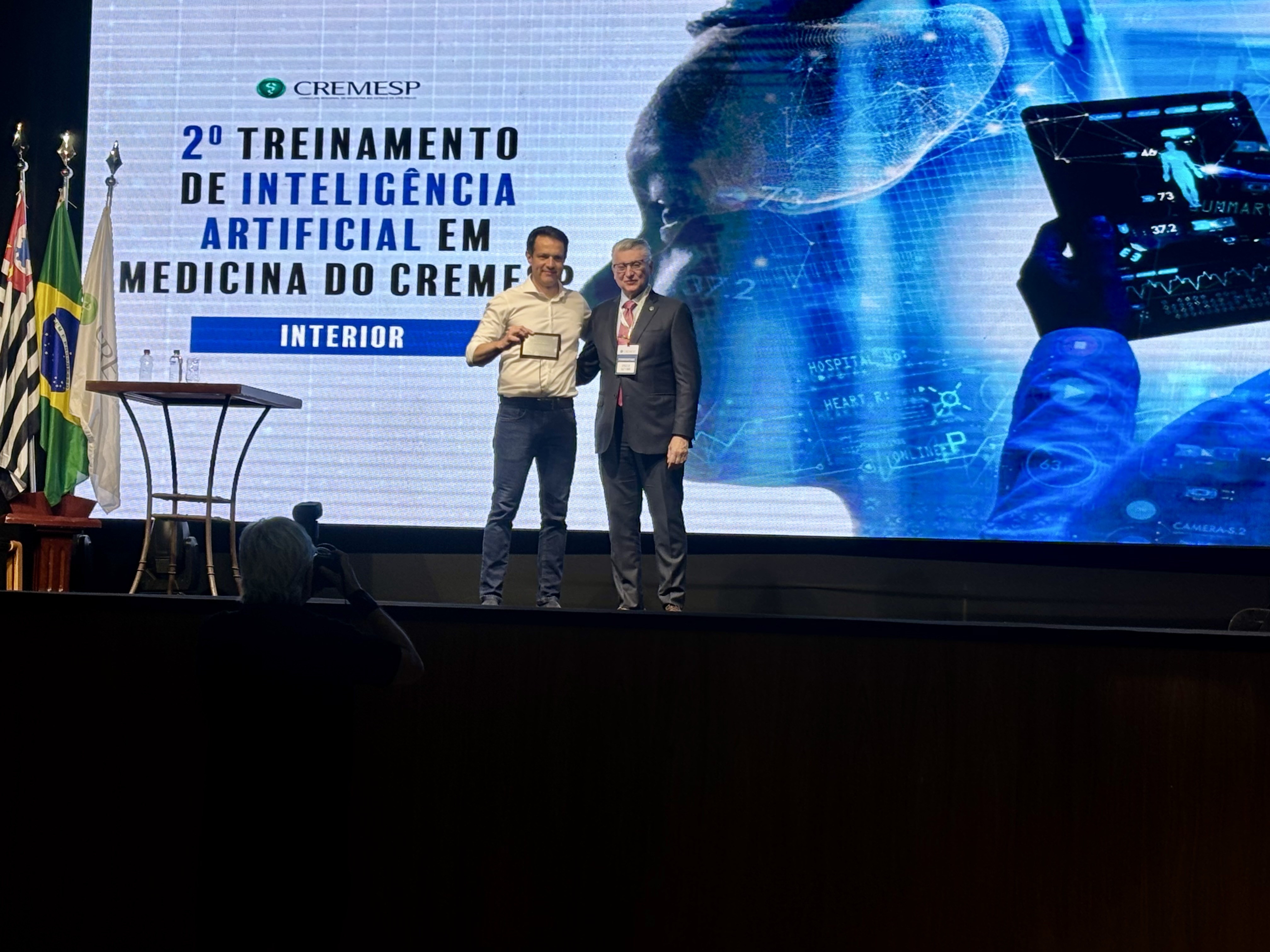 Augusto Salomon recebendo placa de homenagem no palco do 2º Treinamento de IA em Medicina do CREMESP